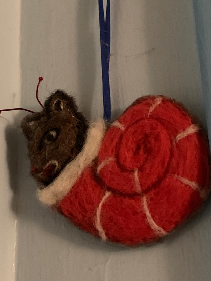 A felted ornament made to look like a snail from illuminated pages.